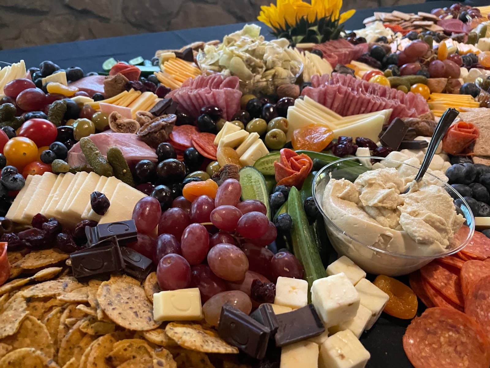 A colorful custom catering board with flowers, fruit, cheese, and charcuterie.